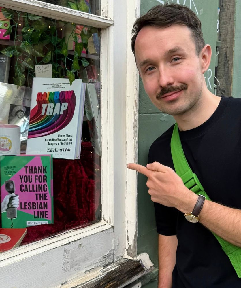 Kevin wearing a black t-shirt standing outside Lighthouse Bookshop. He is pointing at his book Rainbow Trap.