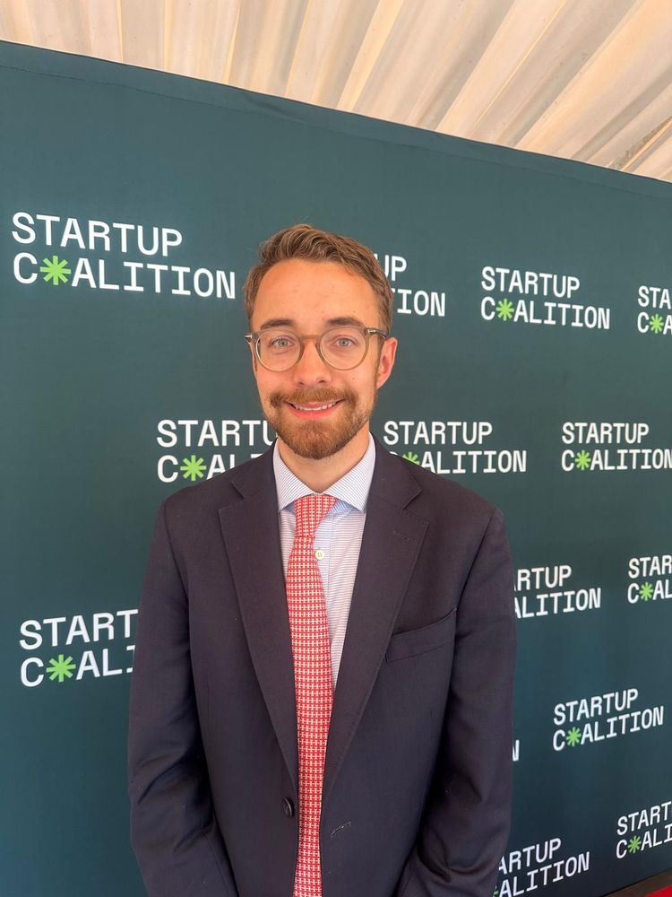 Luke smiling with a Startup Coalition banner in the background.