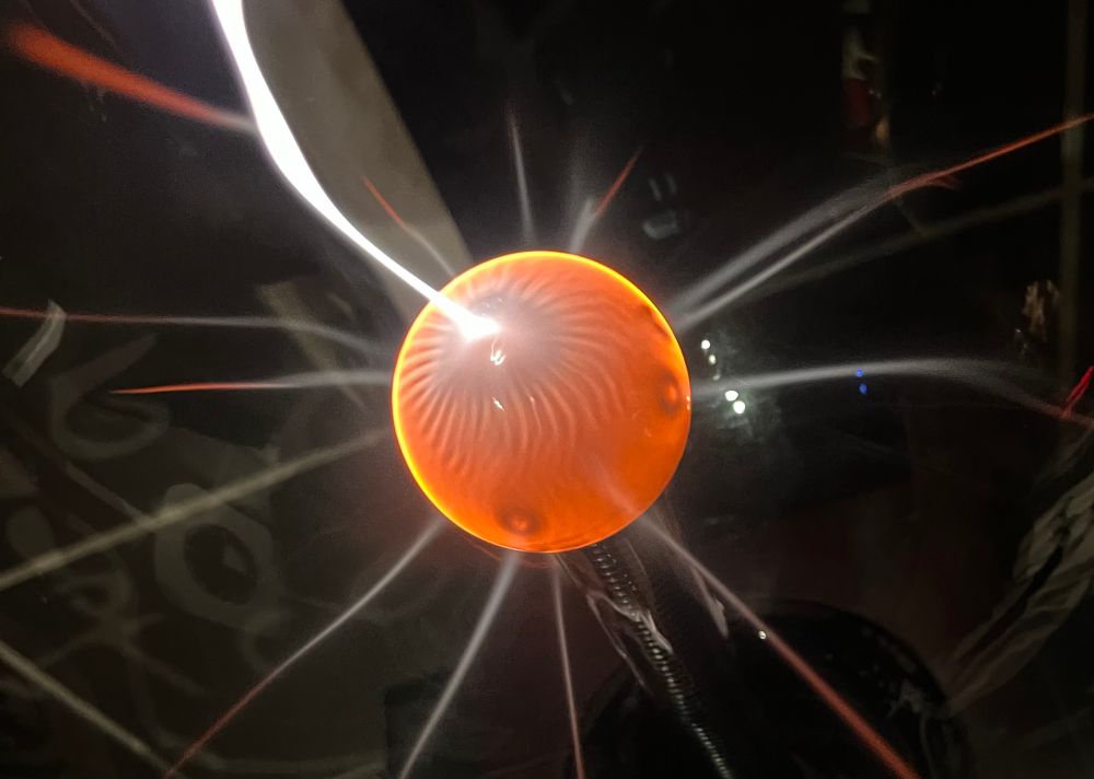 close up of a plasma ball, in the centre a glowing orange ball from which flashes of electricity emanate.