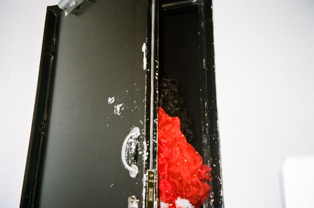 Through the crack of a black stage door a ruffle of red boa peaks through as the performer steps onto stage 