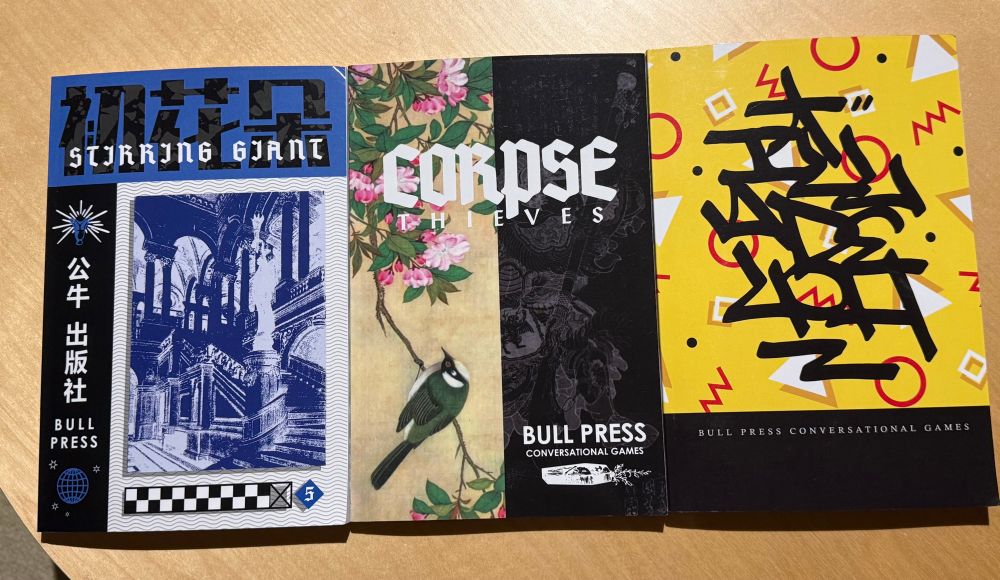 Three book covers:

L: blue and black colour scheme. Book is titled Stirring Giants. Washed out picture of an old building interior
Middle: Corpse Thieves. Right side of cover is black. Left side is image of bird on branch looking up at flowers. 
R: Yellow cover with black band at bottom. Shapes and squiggles in the yellow section of the cover. Title is Illadelph