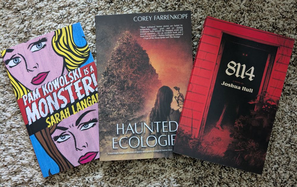 Three books on a carpeted floor. Pam Kowolski is a Monster by Sarah Langan, Haunted Ecologies by Corey Farrenkopf, and 8114 by Joshua Hull