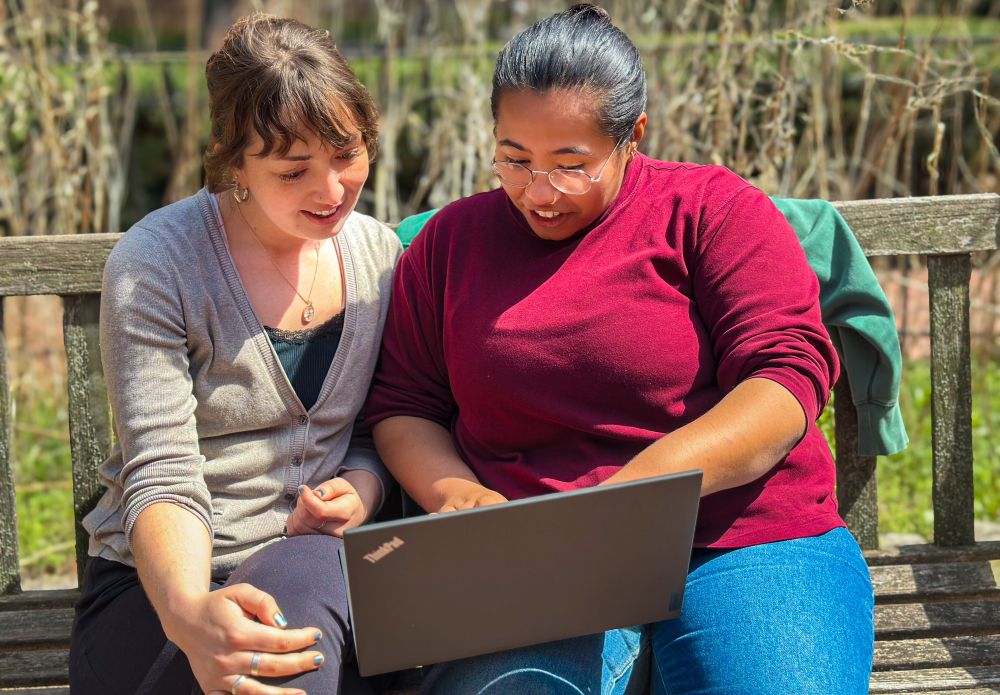 Two members of Programs and Religious Life Staff at Philadelphia Yearly Meeting, sitting on a bench looking at a computer screen. 
