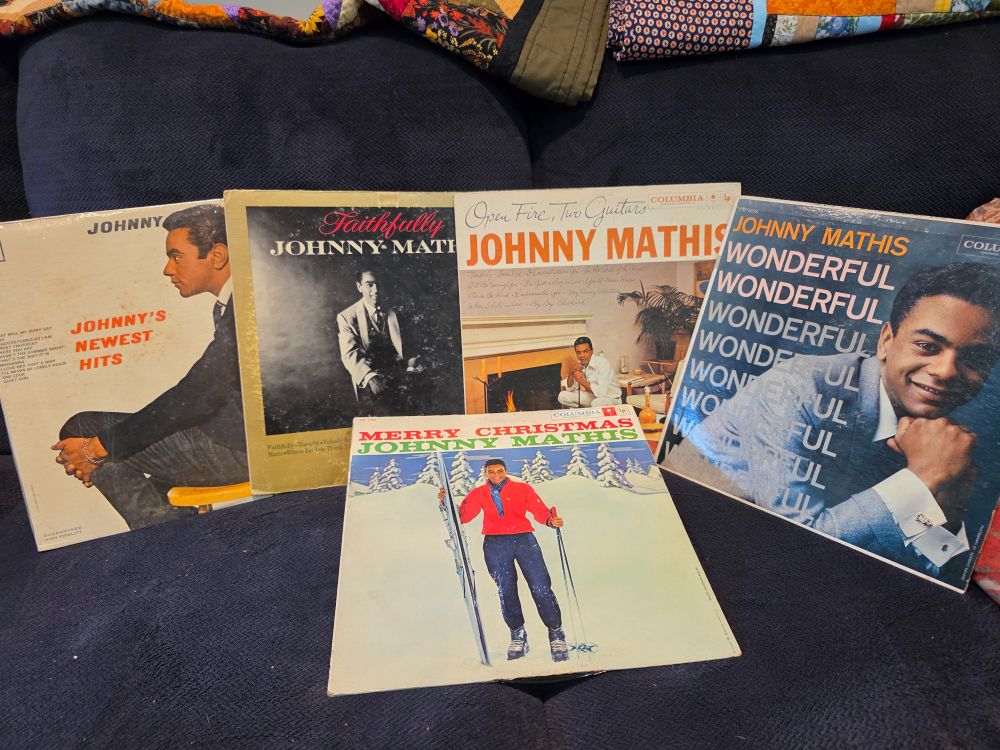 Five Johnny Mathis vinyl albums on a blue couch.