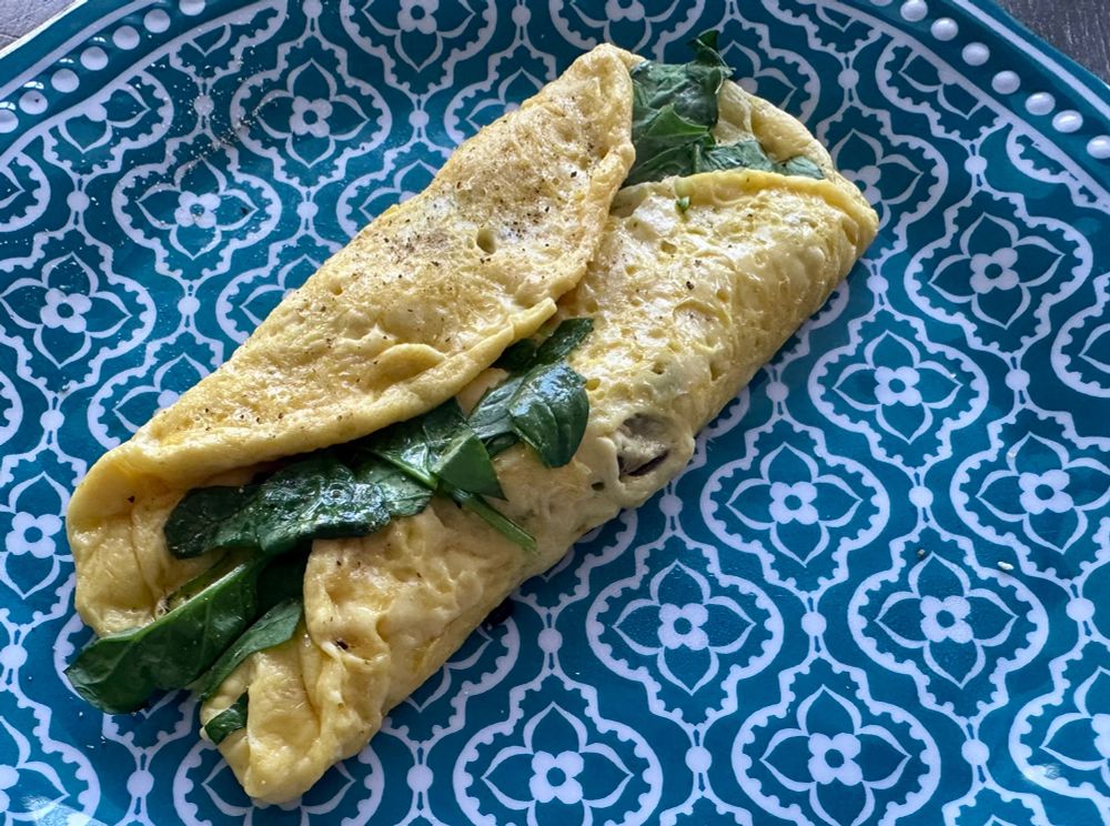 A tri-folded omelette with spinach on a blue plate. 