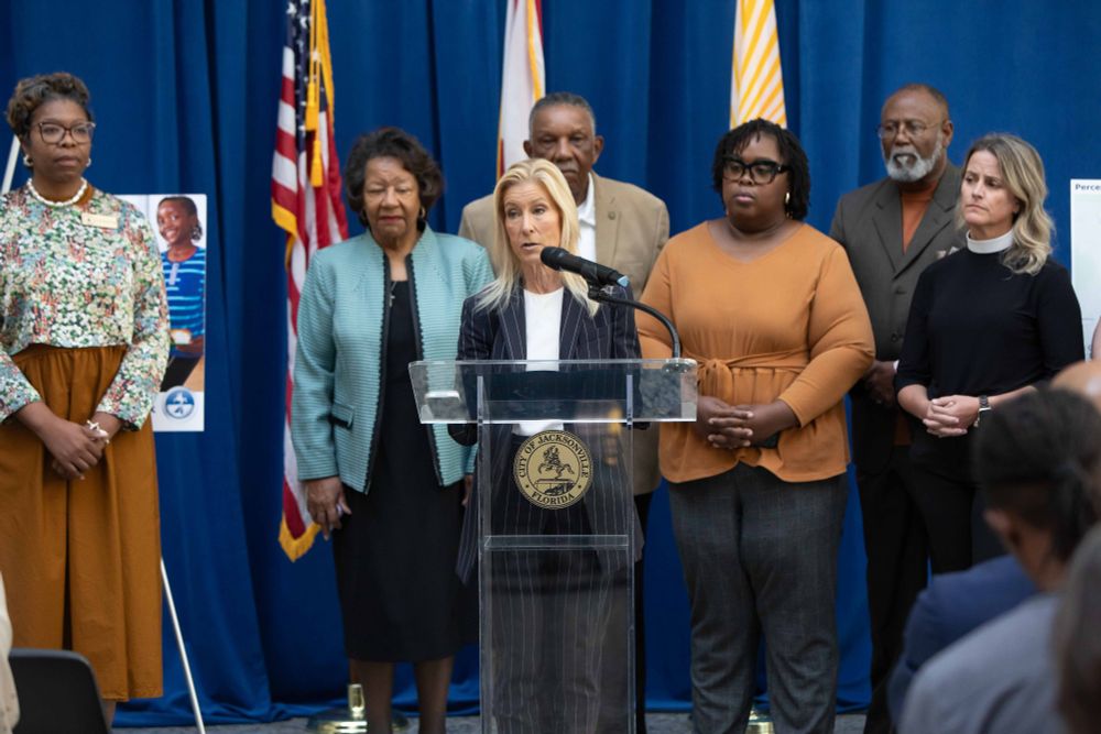 Mayor deegan speaking from behind a podium with members of faith based organizations, city, and non-profits that formed the Duval Cares Coalition to battle hunger needs 