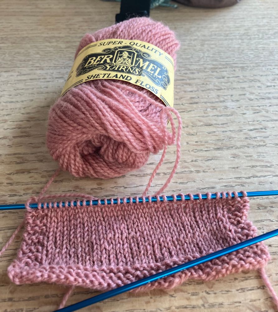 A picece of pink knitting on a wooden table. 