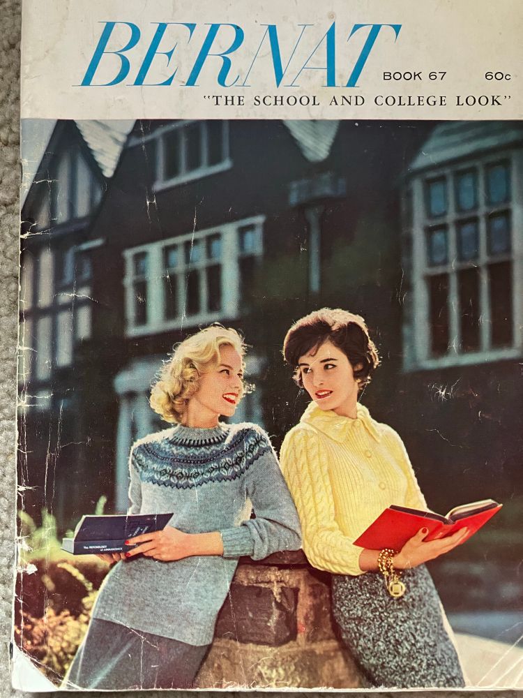 A 1956 knitting pattern book from Bernat yarn. Two  young white women lean on a stone wall holding books and looking at each other. 
