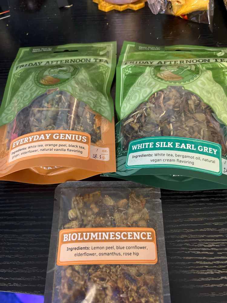 Two bags of loose leaf tea and a small single serving sitting on a black desk 