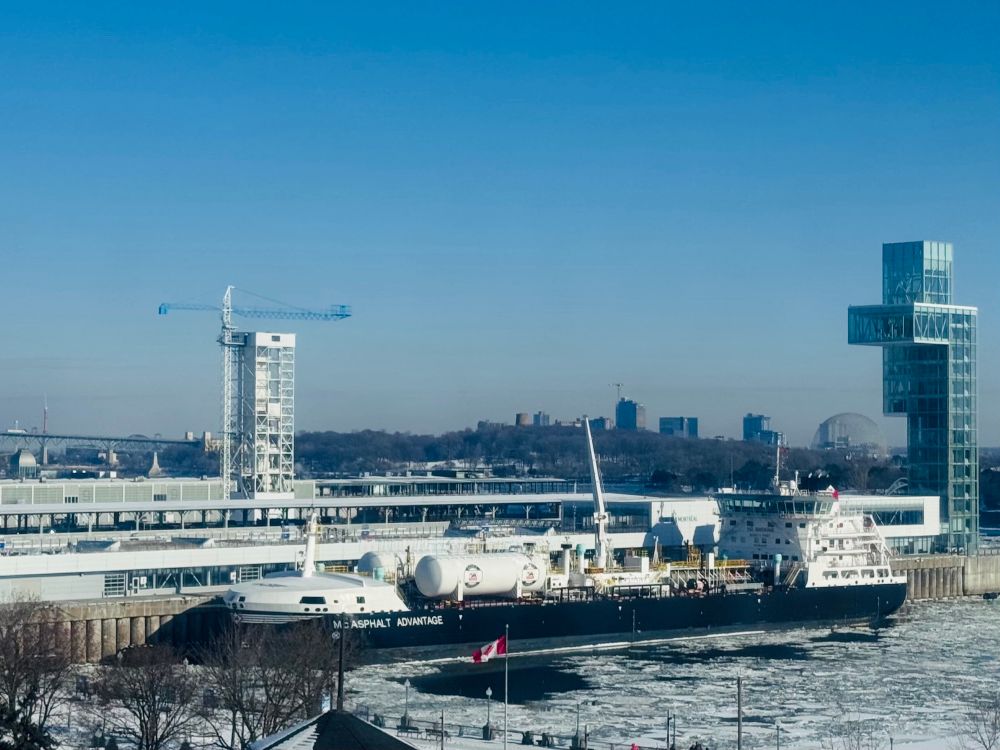 Old Port of Montreal with a large tanker, black base and white storage and navigation areas. Surrounded by broken ice. 