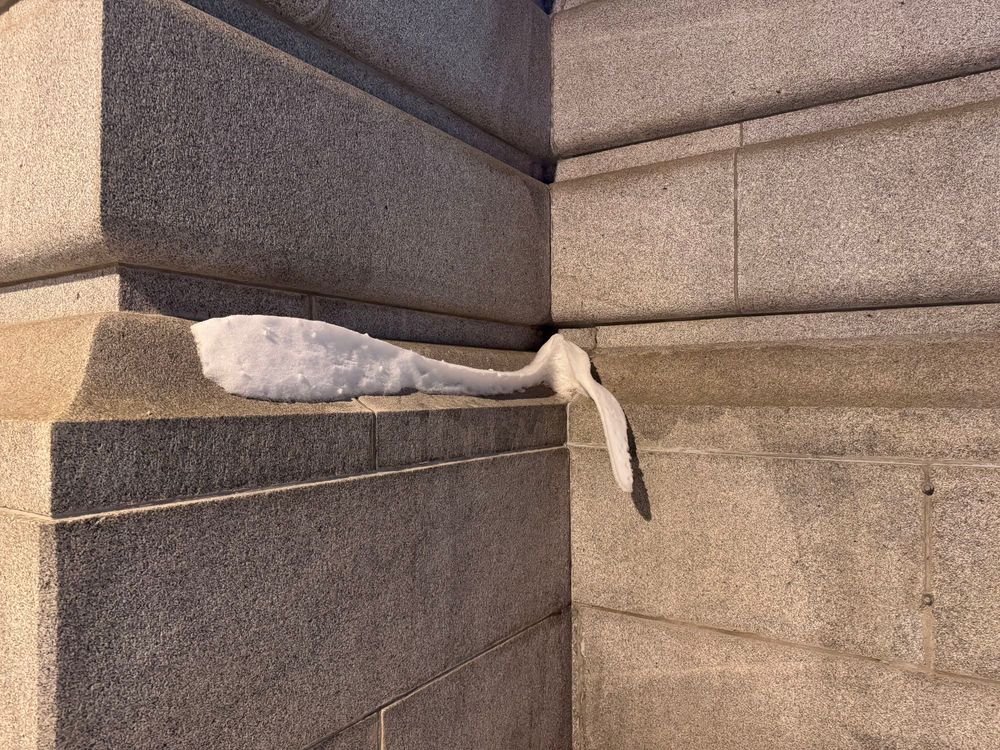 Grey stone wall with a ribbon of snow that has partially curled out and down.