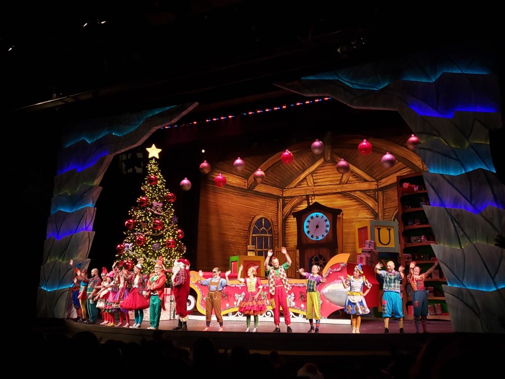 The bows with the cast of Tinker's You Factory show at Canada's Wonderland with a giant Christmas tree on the left and decorations all around and Santa amongst the lineup. 