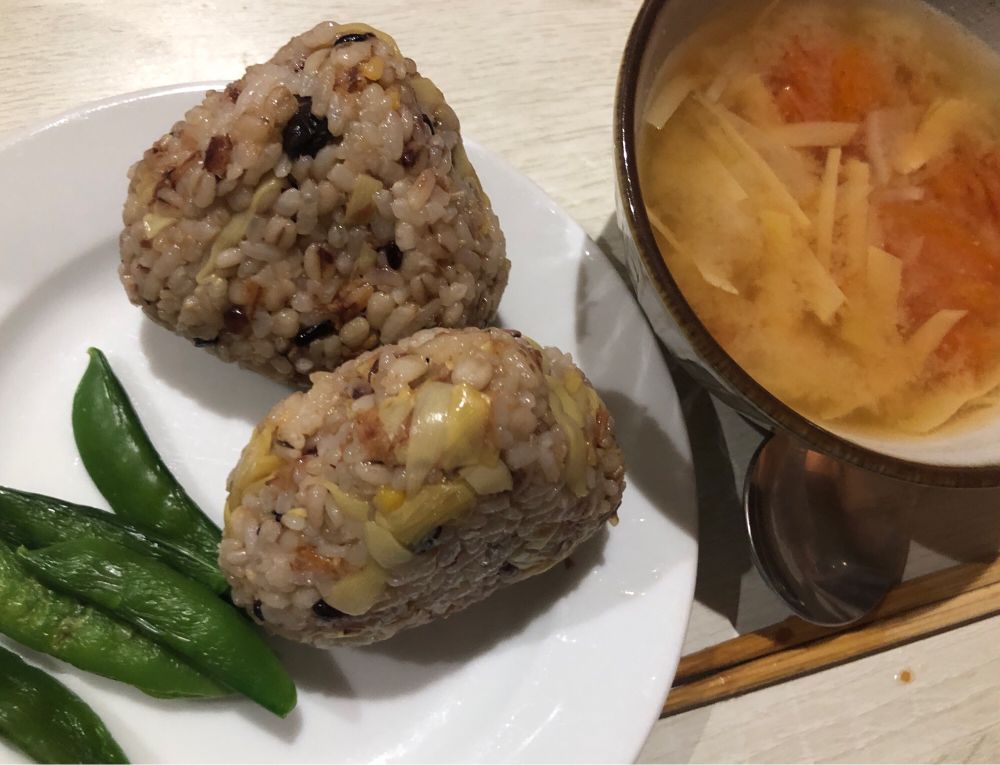 白い正円のお皿の上に、スナップエンドウとたけのことかつお節の雑穀米おにぎり
右にはトマトとたけのこと大根の味噌汁