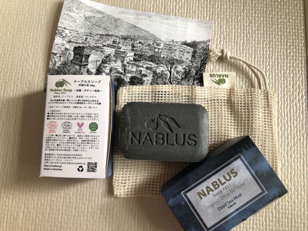 泡立て袋の上に死海の泥の石鹸。それと箱と写真
箱には、赤いECO CERTマークと黒いECO CERTマークとクルエルティフリーのうさぎのマークと緑の八角形のハラールのマーク