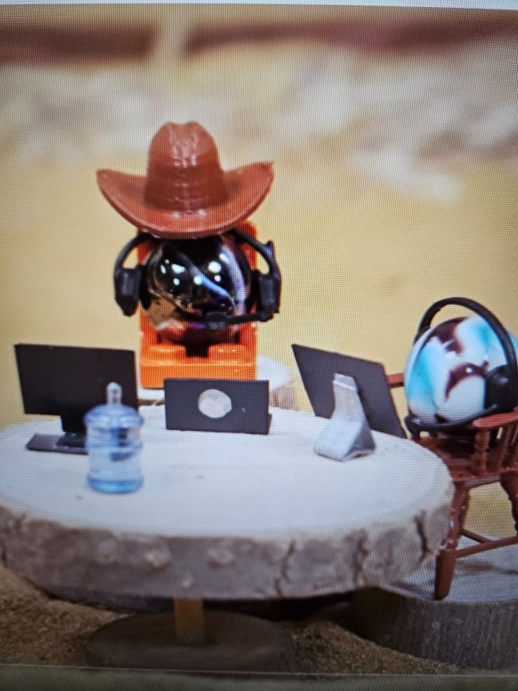 A black marble and a blue and white swirled marble sit in chairs at a table. They are wearing headsets and have tiny computer screens in front of them. The black marble is wearing a ten gallon hat.