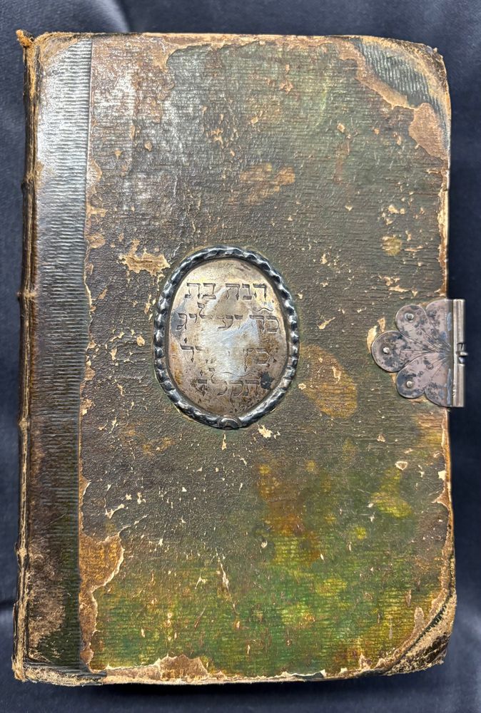 Upper cover of the book bound in parchment that has been colored in green. In the middle you see a center piece furniture with an inscription. The book also contains a metal clasp on the right.