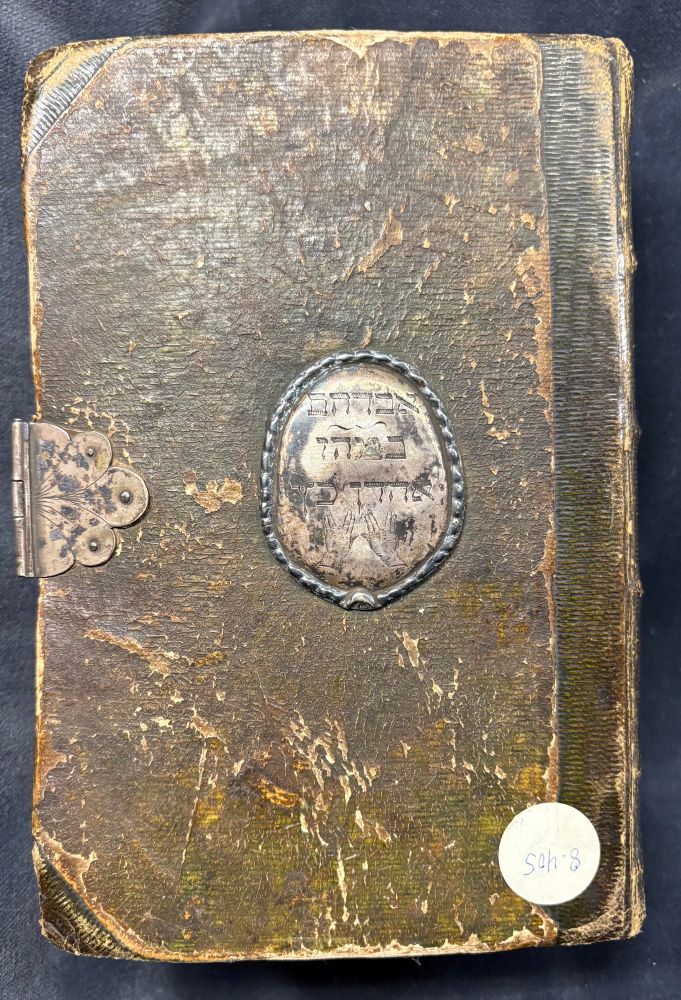 Lower cover of the book bound in parchment that has been colored in green. In the middle you see a center piece furniture with an inscription. The book also contains a metal clasp on the left.