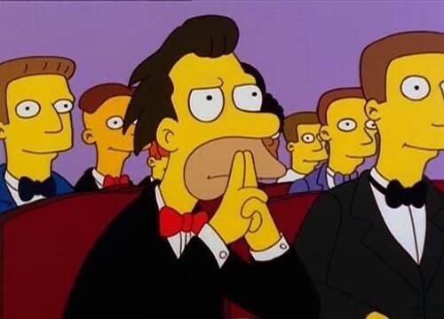 Lenny from The Simpsons sitting in a tuxedo with his pointer fingers held up staring intensely 