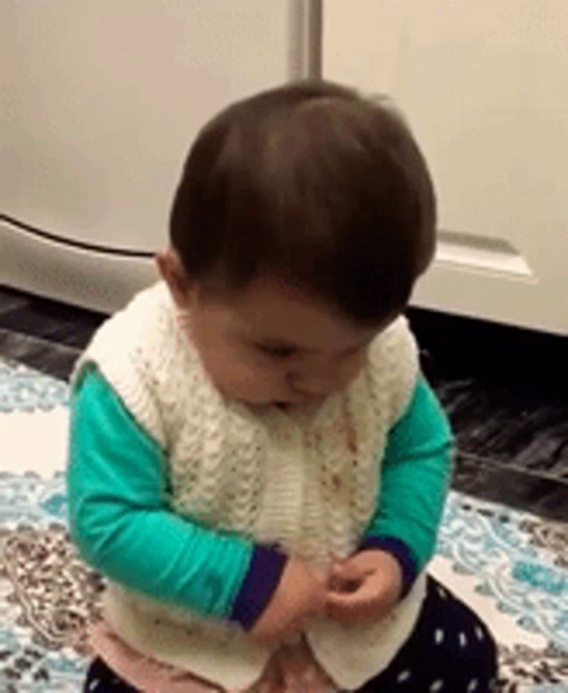 a baby wearing a white vest and green sleeves is sitting on the floor .