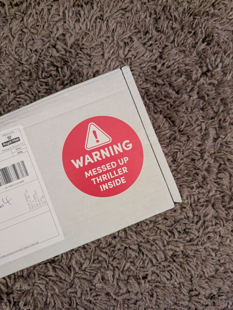 Box with sticker reading Warning Messed Up Thriller Inside lying on rug.