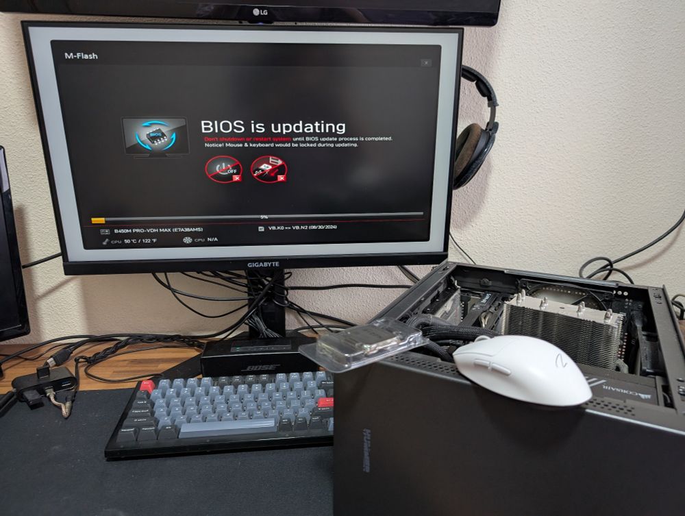 my desk showing a computer on its side with a ryzen CPU tray and a mouse sitting on top as well as a monitor showing a bios update screen