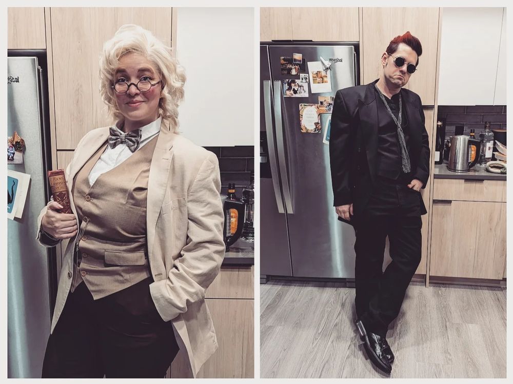 Left, Lana stands in her kitchen dressed as Aziraphale as depicted in the show Good Omens: brown vest, brown plaid woolen tie, short blonde hair and a tan overcoat. She dons petite reading specs and carries a worn old book with a burgundy cover and gold lettering on the spine.

Right, Jeff stands aloof as Crowley. Black jacket, black vest, black pants, and a slim silver decorative scarf. He sports a grimace beneath dark sunglasses and a scarlet pompadour.