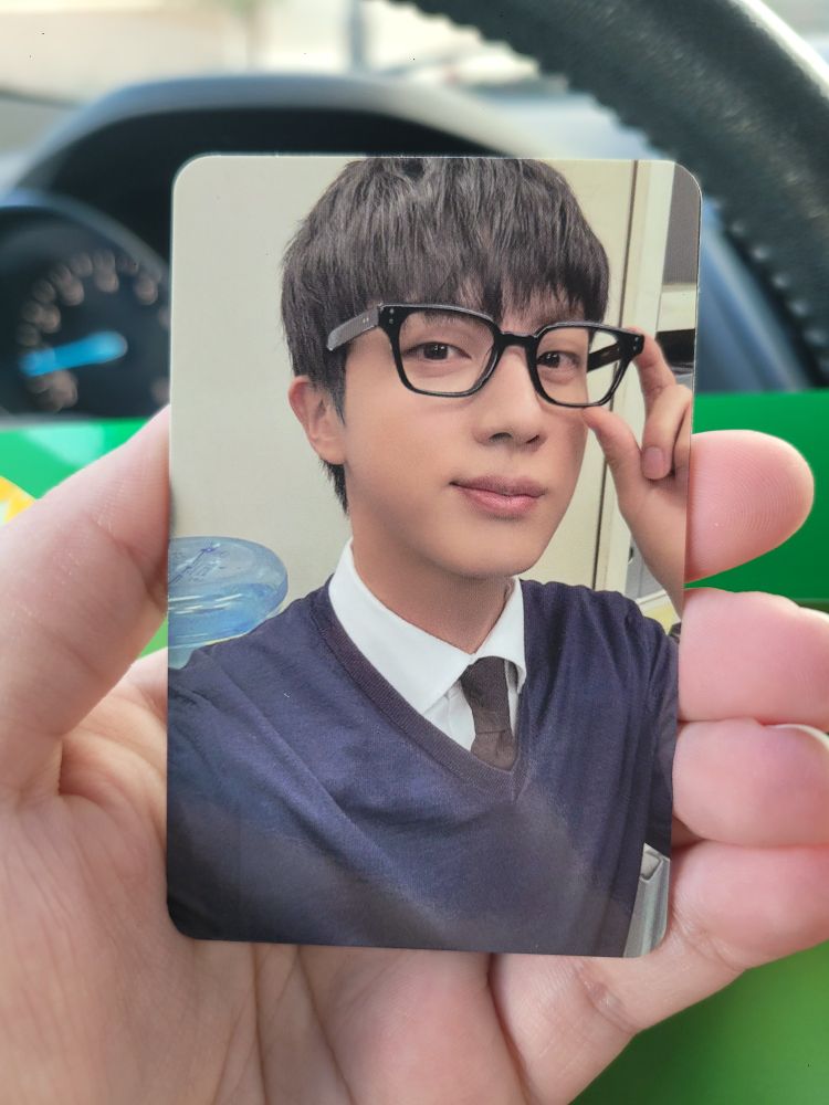 Jin of bts in a blue sweater and thick black framed glasses