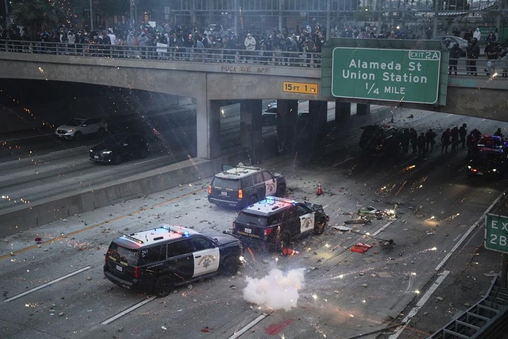 A photograph of police vehicles on a freeway, with protestors on an overpass throwing fireworks below.