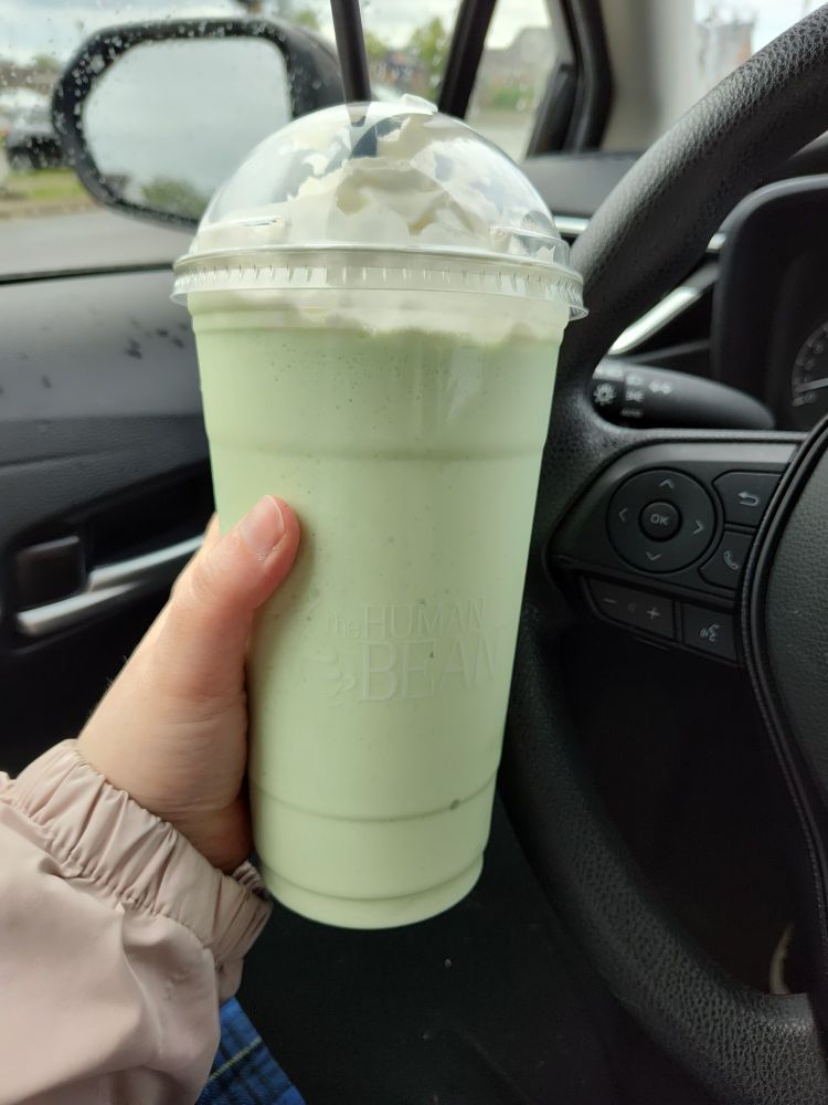 Hand holding up a 32 oz green tea smoothie with whipped cream from The Human Bean 