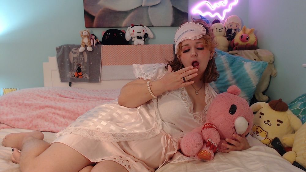 saturn lounging on his bed in a pastel pink frilly vintage pajama set, yawning and holding a gloomy bear plushie.