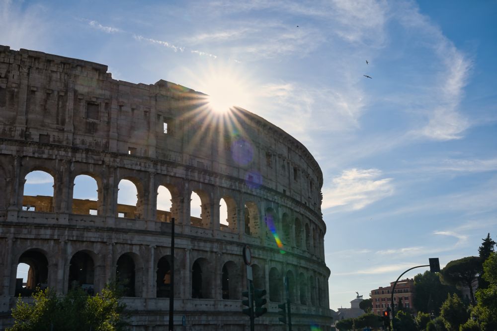 Man siejt das Kolloseum in Rom. Im hintergrund sind auch Häsjer zu sehen die im vergleich recht klein sind. Ausserdem scheint die Sonne über das Kolloseum.