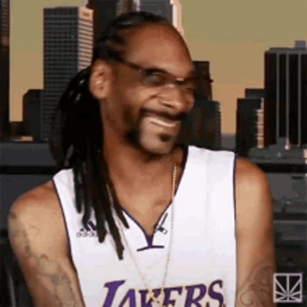 snoop dogg is wearing a lakers jersey and smiling while sitting in front of a city .