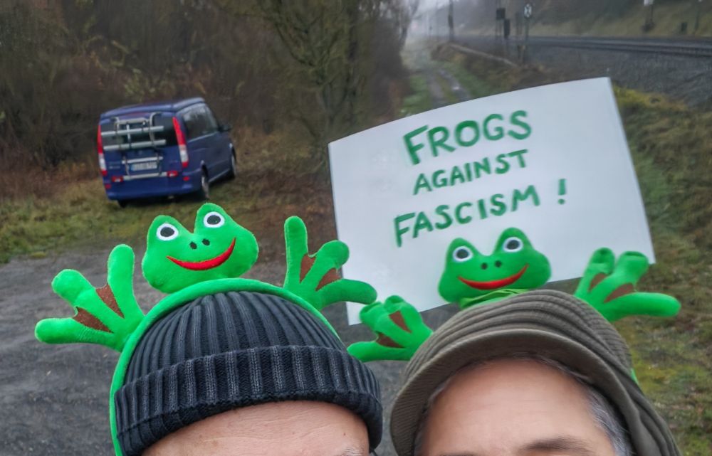 Die Userin und eine weitere Person mit Frosch-Haarreifen auf den Mützen. Der rechte Frosch hat eine Pappe mit der Aufschrift "Frogs Against Fascism!" an den Händen.