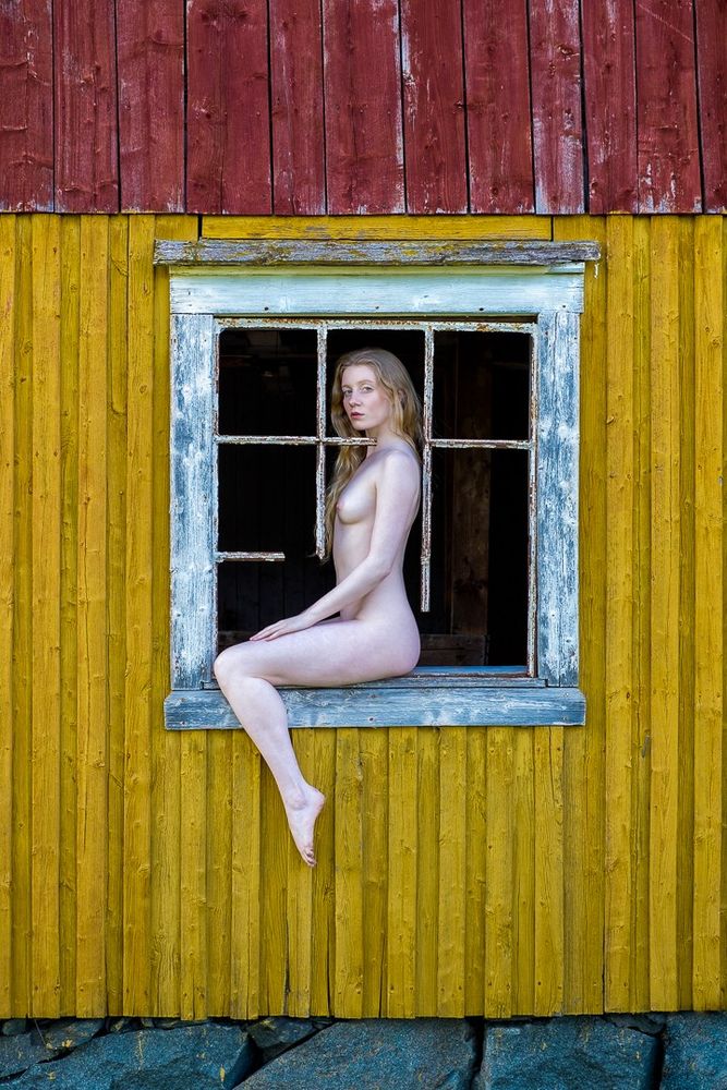 Nude woman posing in window frame of derelict farmhouse