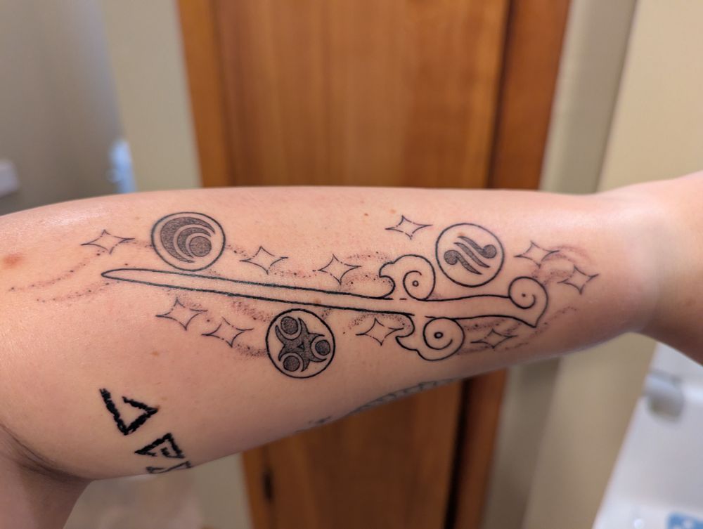 Another angle of tattoo of wind waker baton from the video game The Legend of Zelda The Wind Waker. Around it are goddess pearls with various symbols and shapes repeating wind and sparkles.