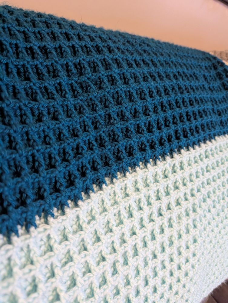 A close up side view of the dark and light blue sections of a waffle stitch blanket which accentuates the waffle stitches.