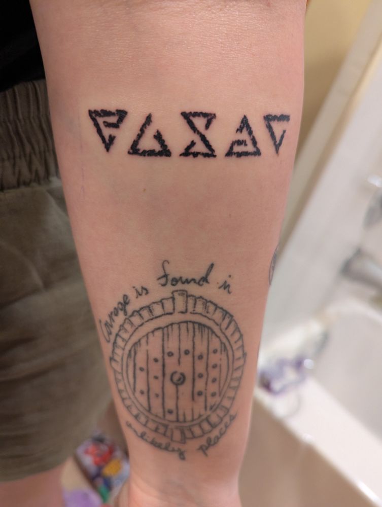 Forearm tattoo of runic signs from The Witcher games above a Hobbit door tattoo.