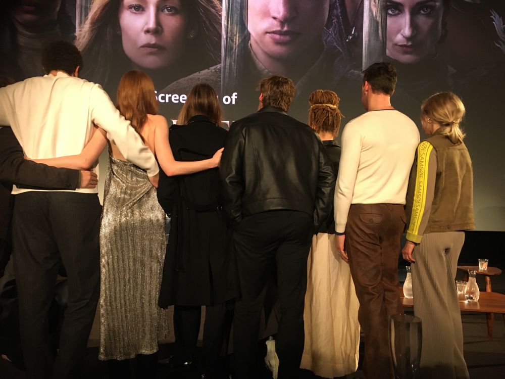 The backs of the extended Wheel of Time cast who attended, taking a group selfie in front of the cinema screen.