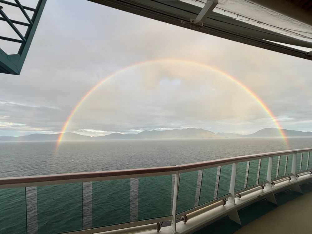 Ship deck with a double rainbow in the water and Alaskan mountains behind it 