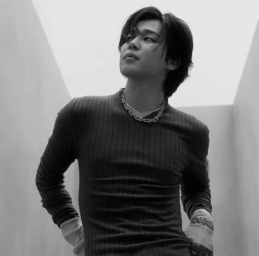 A black and white photo of Park Jimin of BTS posing in a dark long-sleeved shirt.