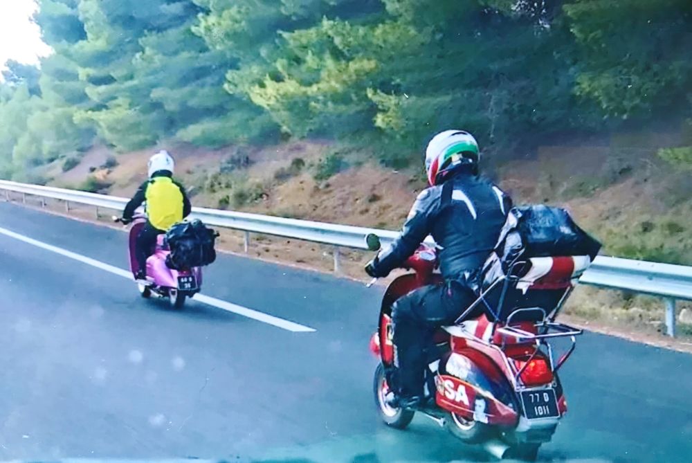 Two vespa scooters traveling on a motorway 
