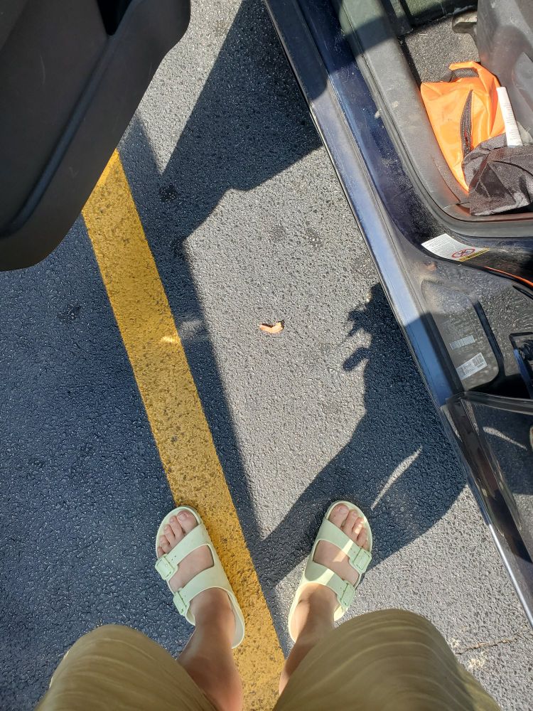 a picture of me standing next to my car in a parking lot with the car door open. the camera is pointed down to the ground, on which there rests a single shrimp tail.