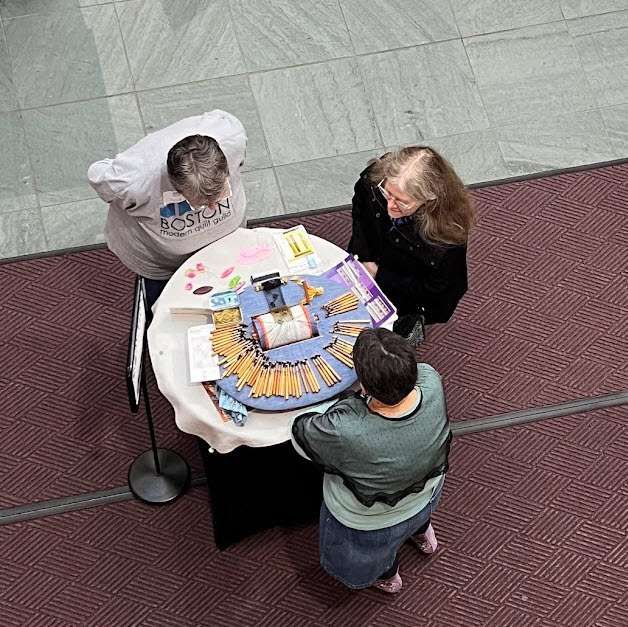 A shot of me talking with two people about bobbin lace from above the atrium where I'm standing. 

My lace pillow is there with about 80 bobbins splayed out and a piece of black silk Ipswich lace being made in the center.