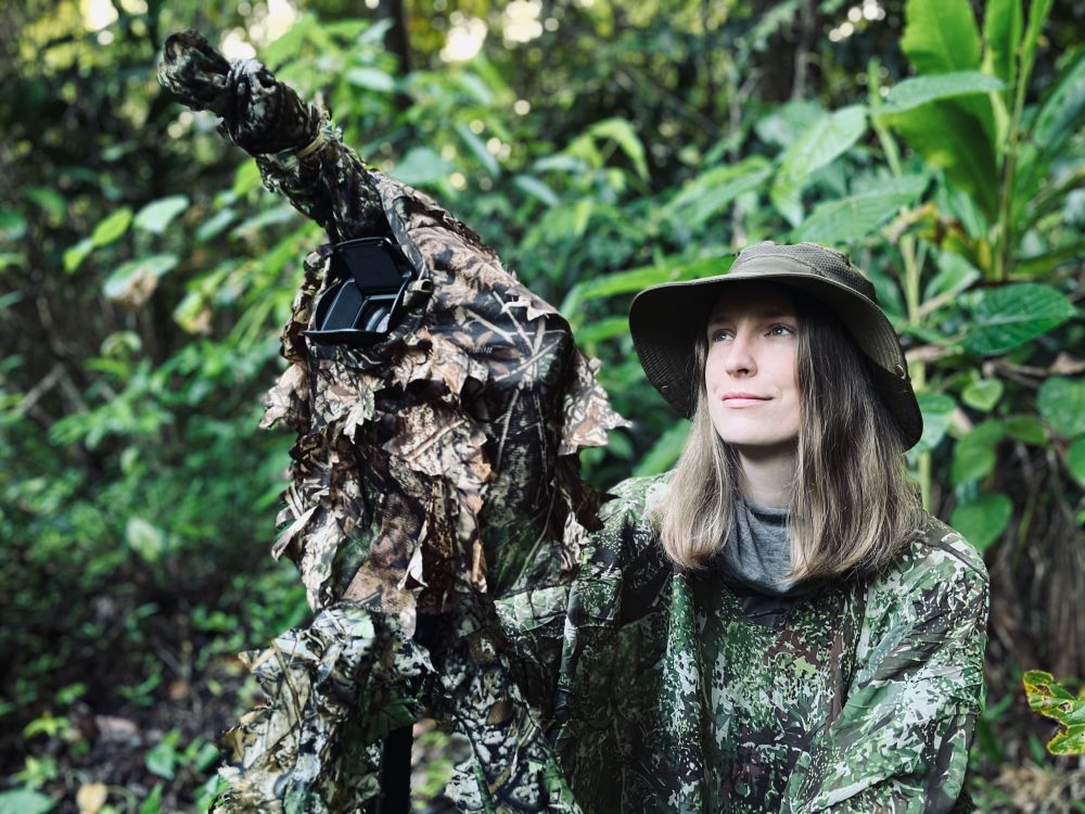 Berenika watches wild cockatoos (not in shot) with camera equipment. Everything is fully dressed in camouflage.