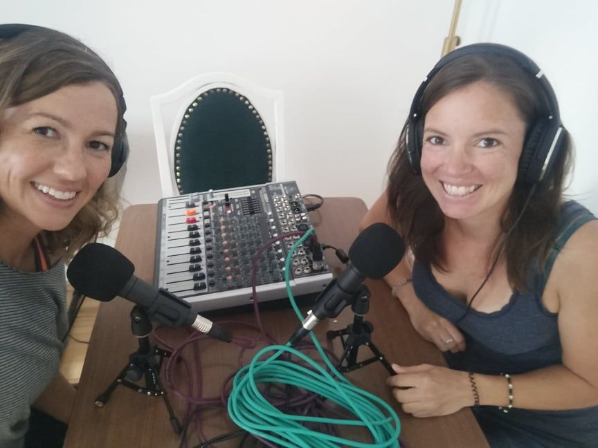Megan and Rachel sit at a table with microphones and audio mixing equipment. Both are excited to be podcasting. 