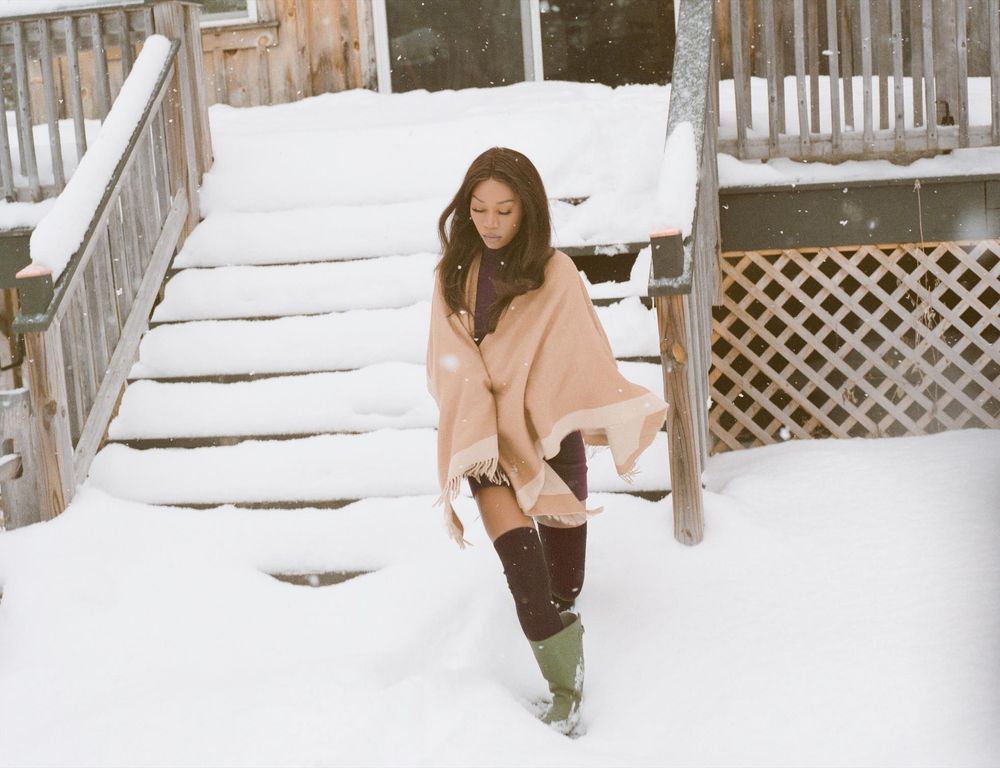 Vanniall stands in front of a snow-covered staircase, wrapped in a tan shawl. The cold air is blowing through her hair.