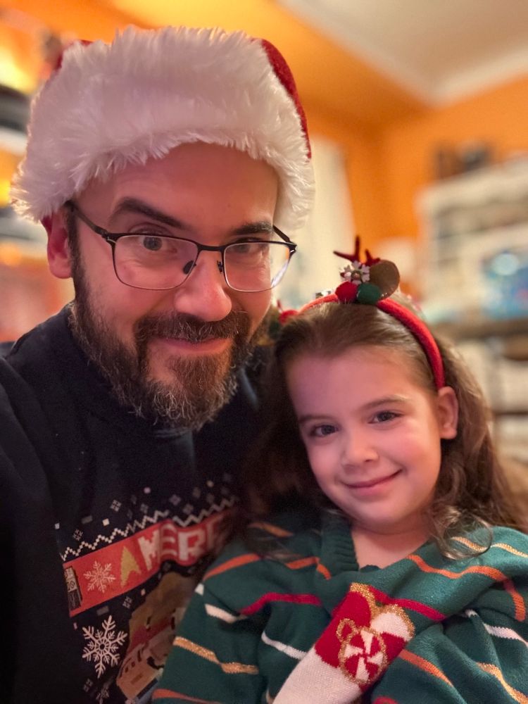 The same bearded be-Santa-hatted JCW but smiling with a lil reindeer child.