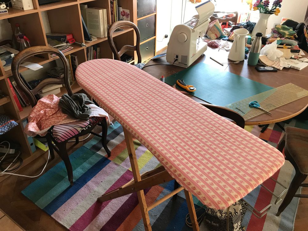 Une table à repasser au premier plan, et une table avec une machine à coudre au deuxième plan.