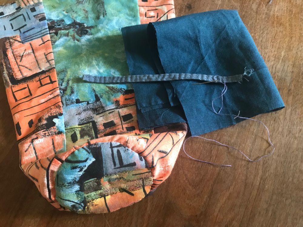 Sewing work in progress : a pouch is on the table. The quilted bottom is finished. A blue fabric is waiting to be sewn at the top. A threaded sewing needle is close to a hand stitched band that will be used to fix the pouch to a bag.
#bag #sewing #handsewing #sewsky #vintagefabrics