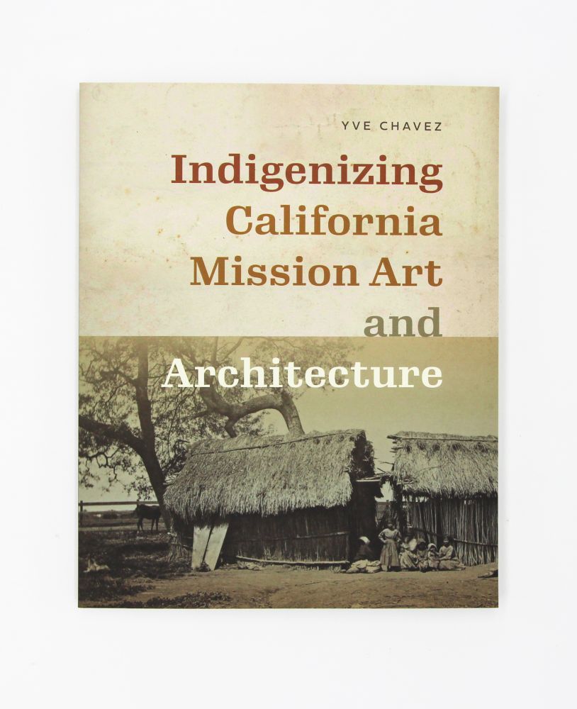Book cover of Indigenizing California Mission Art and Architecture by Yve Chavez. The title is in bold, warm-toned typography on a beige background. Below the title, a sepia-toned historical photograph depicts Indigenous people sitting in front of thatched-roof structures under large trees, suggesting a connection to Native Californian life and built environments.